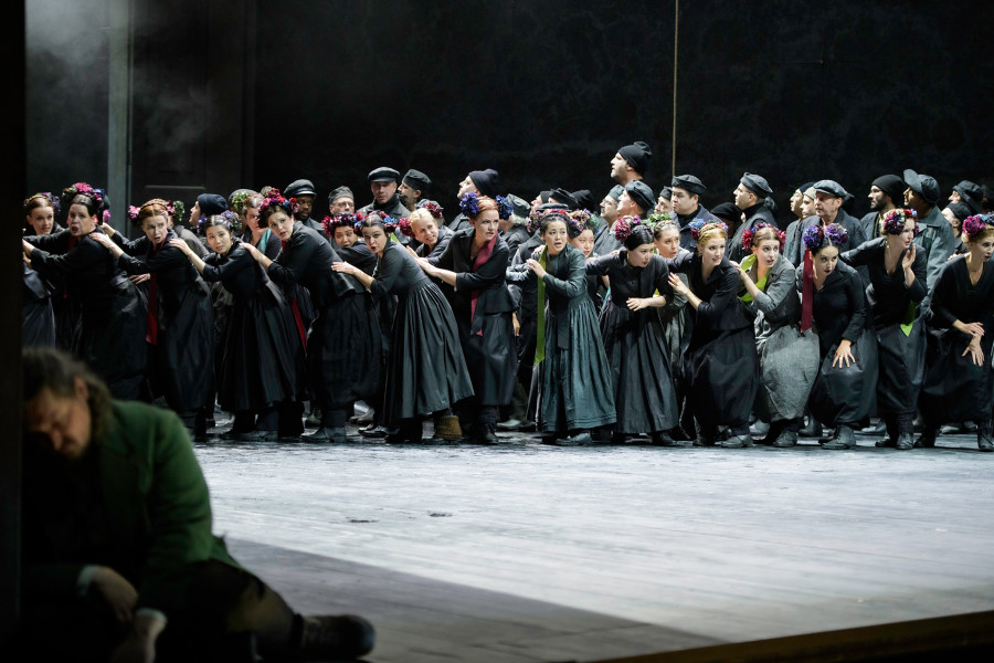 Der fliegende Holländer - © Bettina Stöß In einer Choreografie tanzen die Seeleute und ihre Frauen. Als Farbtupfer an den schwarzen Kostümen der Frauen sind bunte Blumen auf Hüte und in Frisuren gesteckt. Abgewandt sitzt immer noch Erik am Portal.