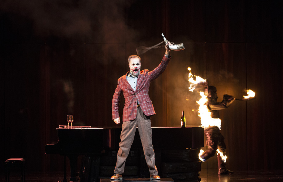 Götterdämmerung - © Bernd Uhlig Hagen hat Siegfried getötet. Nun hält er als Trophäe dessen Horn in der Hand. Hinter ihm läuft ein brennender Mann über die Bühne.
