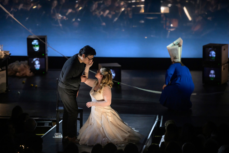 Aida - © Bettina Stöß Aida kniet vor Radames, dessen Wange sie zärtlich berührt. Im Hintergrund abgewandt Amneris.