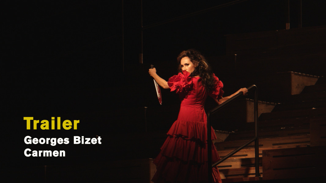 Georges Bizet: Carmen (2024) - © Ruth Tromboukis Dieses Foto ist ein Standbild zum Videotrailer mit Stückimpressionen aus Ole Anders Tandbergs Inszenierung von CARMEN. Carmen steht in einem tiefroten Flamencokleid im Treppenrund der Arena und hält ein großes Messer in der Hand.