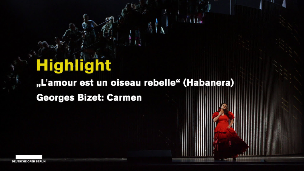 Die Video-Reihe „Highlights“ präsentiert künstlerische Höhepunkte aus verschiedensten Werken. Hier singt die französische Sopranistin Clémentine Margaine die Habanera „L'amour est un oiseau rebelle“ aus Bizets CARMEN. Wir befinden uns im ersten Akt der Oper. Eine Wand aus Wellblech dreht sich Richtung Hinterbühne und gibt den Blick frei auf ein großes Arena-Rund. Auf den Stufen der Arena sitzt und steht der Chor, der sich im Verlaufe des Habanera begehrlich um Carmen schart. Vor der Bühnenkonstruktion geht Don José vorbei und reizt Carmen dadurch, dass er sie nicht beachtet. Carmen trägt ein sehr auffälliges knallrotes Flamencokleid, Don José so wie der Herrenchor Kleider aus Armee-Kaki, die Damen des Chores tragen Alltagskleider in eher gedeckten Farben.