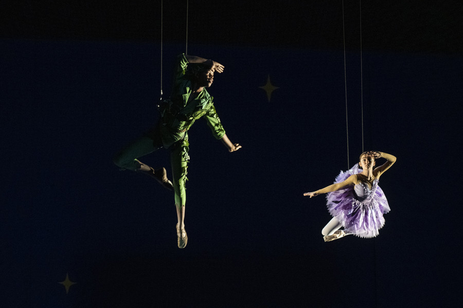 "Kinder tanzen – Peter Pan" ist ein Kinderballett für alle ab 4 Jahren. Es tanzen die Elev*innen der Kinder Ballett Kompanie. Auf diesem Bild in der Flugmaschinerie Peter Pan in seinem typischen grünen Outfit und Tinkerbell in einem lilafarbenen Kleid.