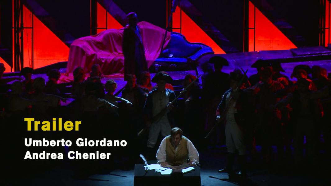 Umberto Giordano: Andrea Chenier – Ein Video-Trailer - © Andreas Bolle Dieses Foto ist das Standbild zum Videotrailer mit Stückimpressionen. Es zeigt eine Situation aus dem letzten Bild. Bereits zum Tode verurteilt, kniet er am Souffleurkasten und schreibt ein letztes Gedicht. Hinter ihm das Volk von Paris und ein Bühnenbild, das mit roten Zacken die brennende Stadt imaginiert.