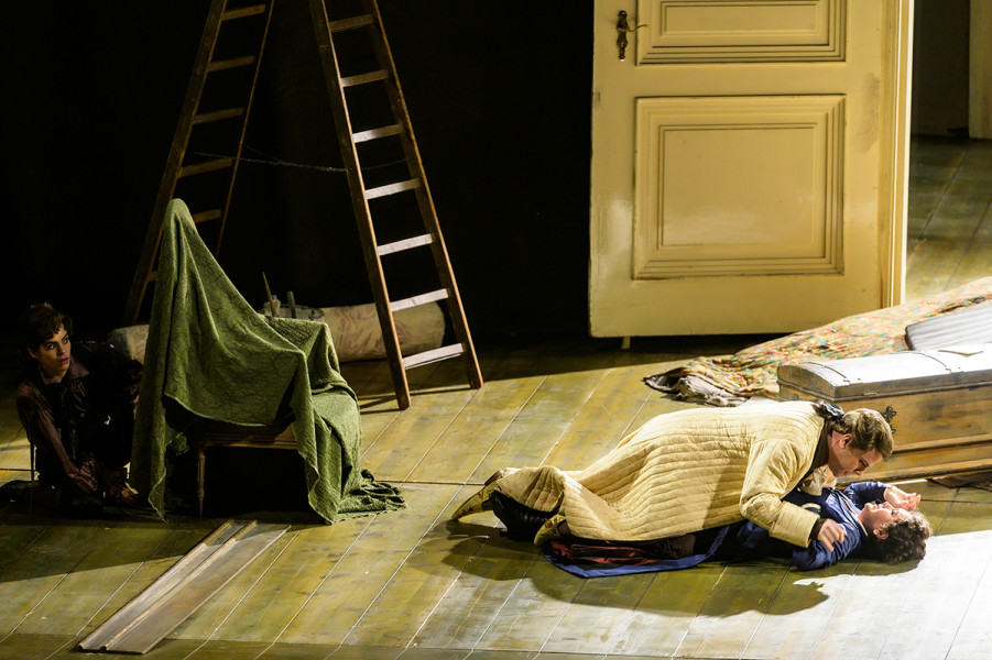Le nozze di Figaro - © Bettina Stöß In einem cremefarbenen Morgenmantel ist der Graf zu Besuch im zukünftigen Zimmer Susannas und Figaros. Er bedrängt Susanna massiv. Beide liegen am Boden, die Gegenwehr Susannas ist wahrnehmbar. Hinter einem Lehnstuhl verborgen ist der Page Cherubino. Er beobachtet das Geschehen.
