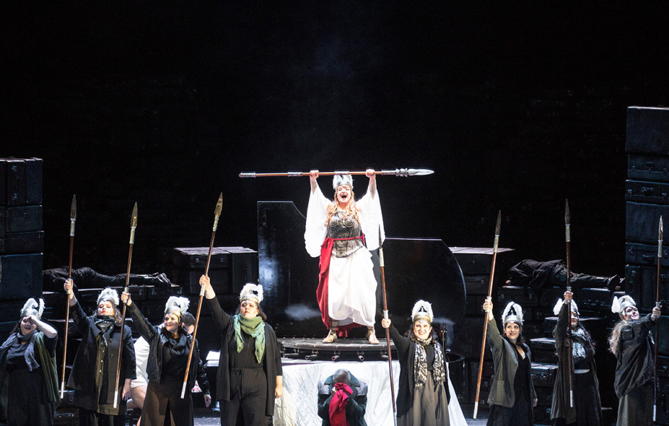 Die Walküre - © Bernd Uhlig Die Walküren treffen sich jauchzend, um mit den eingesammelten, gefallenen Helden nach Walhall zu ziehen: „Hojotoho!“ Brünnhilde steht in mythischem Gewand auf dem Flügel. Ihre Schwestern in langen Mänteln, die noch vom Blut der Schlachtfelder schmutzig sind, umgeben sie. Alle führen sie Lanzen mit sich.