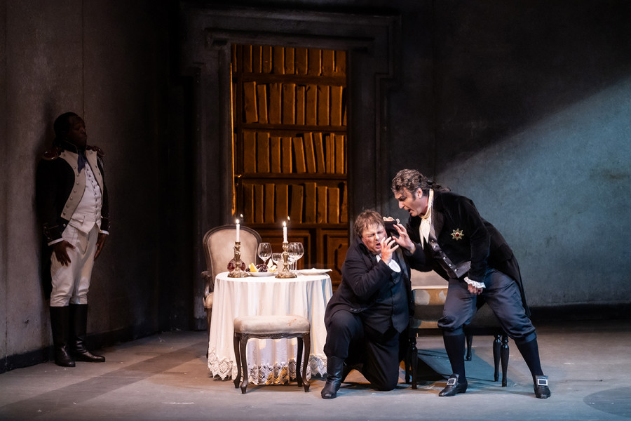 Tosca - © 2023, Bettina Stöß Ängstlich kauert sich Spoletta zusammen. Scarpia, sein Herr, bedroht ihn heftig.