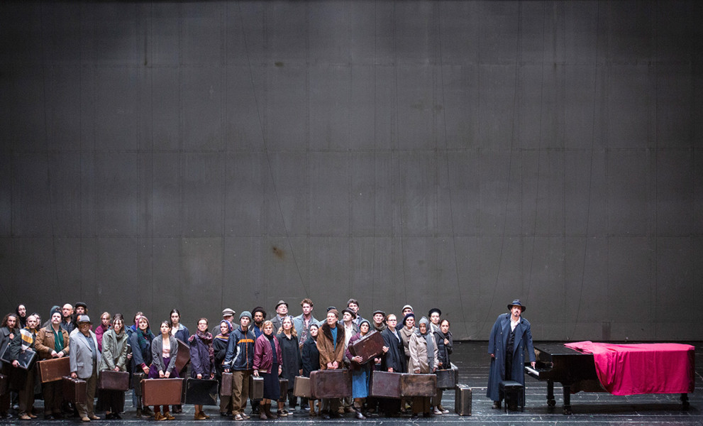Das Rheingold - © Bernd Uhlig Eine Gruppe Flüchtender und Heimatloser betritt die Bühne und trifft auf einen Flügel. Gemeinsam erschaffen sie sich einen neuen Mythos, eine Grundlage ihrer Kultur aus dem Geiste der Musik. Unter ihnen der Mann, der sich in Wotan verwandeln wird.
