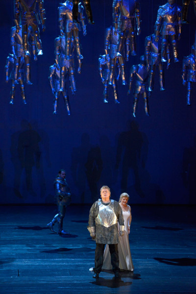 Eingeladen auf die Wartburg treffen Elisabeth und Tannhäuser aufeinander. Im Hintergrund beobachtet Wolfram das Geschehen. Die Bühne ist in tiefes Blau getaucht. Aus dem Bühnenboden hängen viele Ritterfiguren herab.