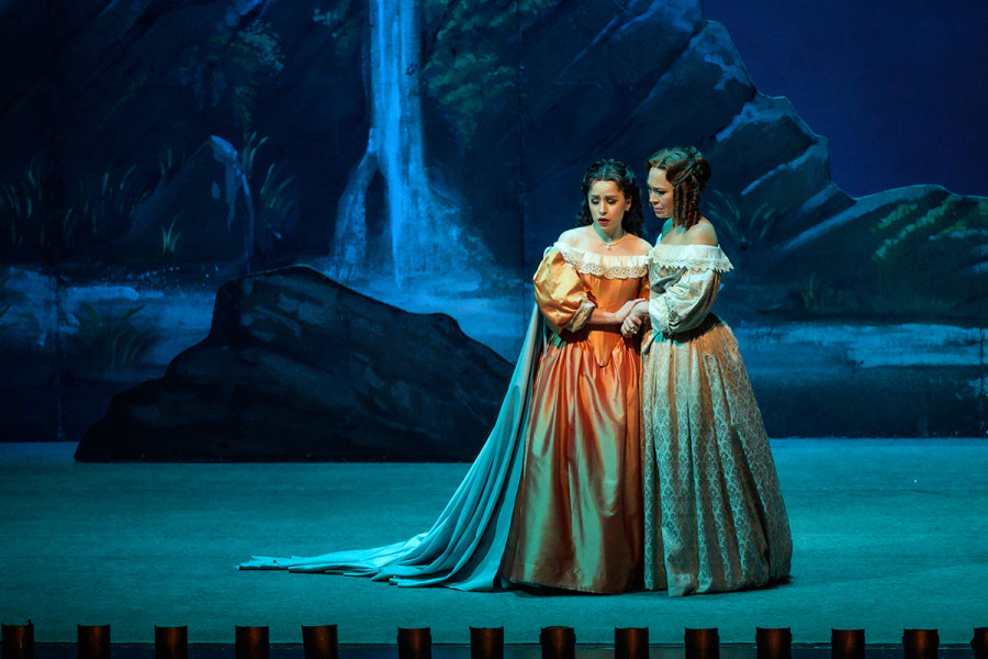 Lucia und ihre Vertraute Alisa stehen in einer mondbeschienenen Nachtszene in einer idealen romantischen Landschaft mit Wasserfall und idyllischen Felsen.