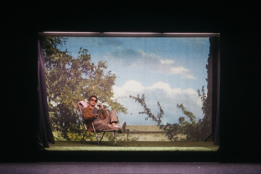 Nikolay Borchev als Ospite sitzt auf einem Liegestuhl vor einer idealen Sommerlandschaft, lesend