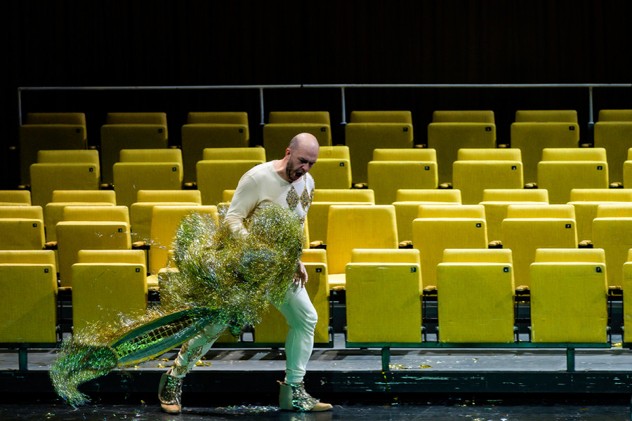Rigoletto - © Bettina Stöß Wütend und verzweifelt wirft Rigoletto sein Goldhasen-Kostüm in die leeren Stuhlreihen. Nun trägt er ein Narrenkostüm mit den typischen Rauten.