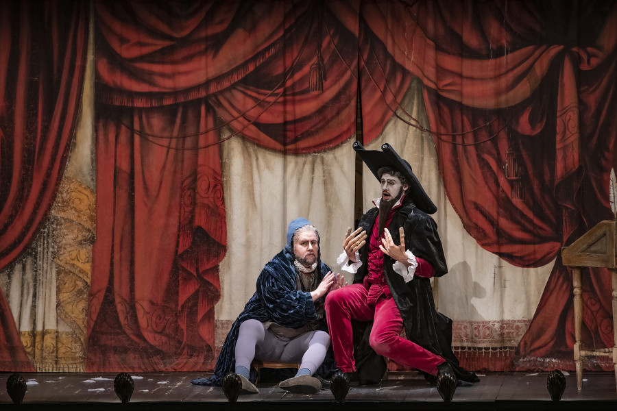 Il barbiere di Siviglia - © Bettina Stöß Vor die Kulisse des gemalten Wohnzimmers hat sich ein ebenso gemalter Bühnenvorhang gesenkt mit vielen Zugschnüren und Raffungen. Davor sitzen Bartolo und Basilio, der sein berühmtes "La Calunnia" singt.