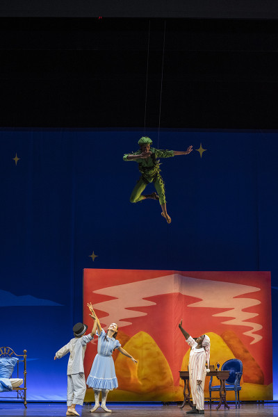 Michael, John und Wendy spielen in ihrem Kinderzimmer. Von oben herab schwebt Peter Pan.