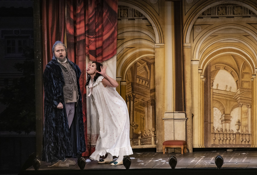 Il barbiere di Siviglia - © Bettina Stöß Der Vormund Bartolo ist ins Wohnzimmer gekommen. Er trägt einen blauen langen Mantel und eine Art Schlafmütze. Rosina streckt ihm die Zunge raus.