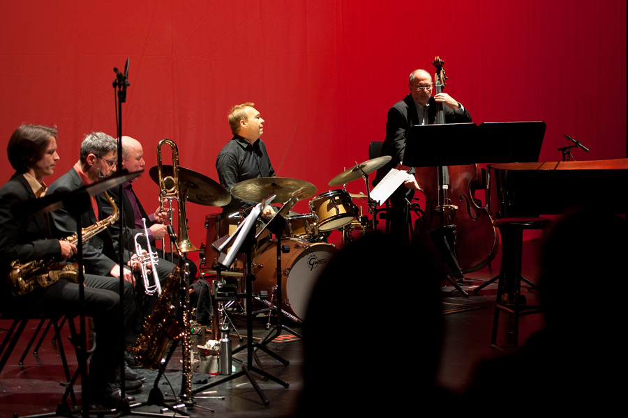 Jazz & Lyrics - © Stephan Bögel Musiker der Bigband bei einem Konzert in der Tischlerei. Der Rücksetzer ist tiefrot angestrahlt.