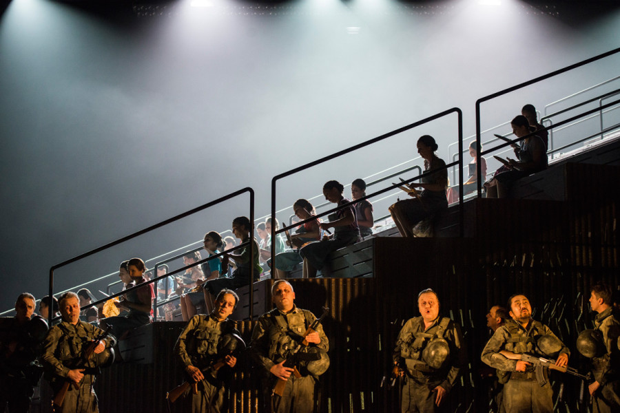 Die Herren des Chores stehen in Militär-Kaki vor dem Arenarund, die Damen des Chores sitzen in blauen Arbeitsschürzen auf den Stufen.