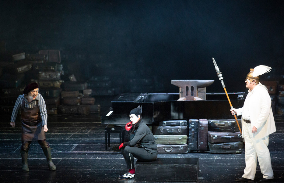 Das Rheingold - © Bernd Uhlig Wotan und Loge treffen auf den geschundenen Mime, der ihnen von Alberichs gewaltiger Macht erzählt. Links steht Mime, auf dem Souffleurkasten sitzt Loge und rechts im Bild steht in den Insignien seiner Macht Wotan.