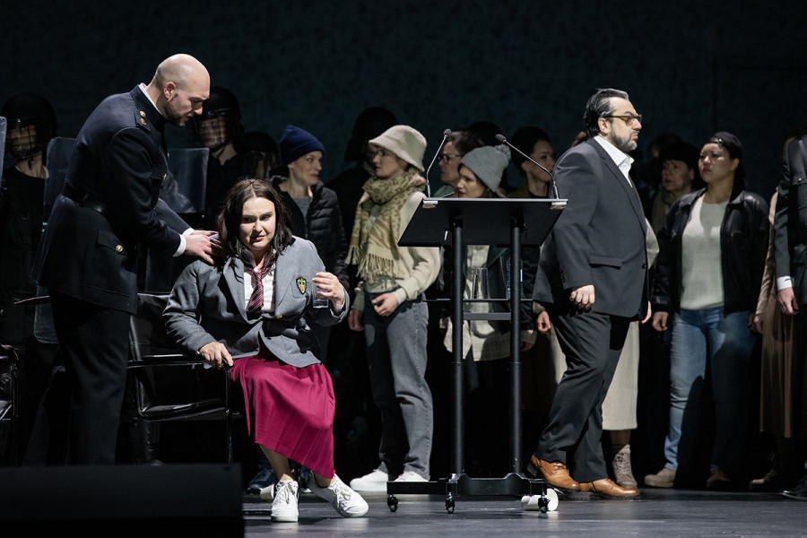 Simon Boccanegra - © Bettina Stöß Gabriele Adorno berührt Amelia, die zusammengesunken auf einem Stuhl sitzt, sanft an der Schulter. Boccanegra geht nach rechts ab. Um die drei die Bevölkerung Genuas.