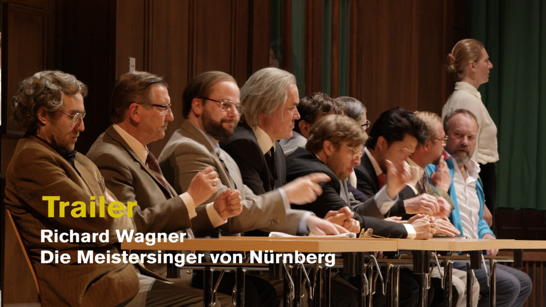 Dieses Bild ist das Standbild für einen Video-Trailer. An einem langen Tisch sitzen die Meistersinger als Jury. Am oberen Ende Hans Sachs.