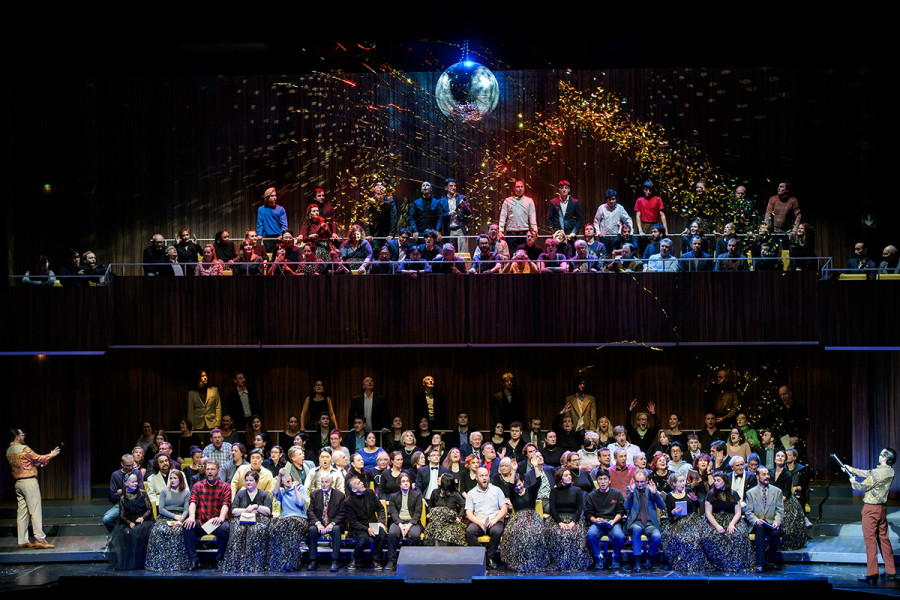 Rigoletto - © Bettina Stöß Der Chor sitzt in den Sitzreihen des auf die Bühne gespiegelten Saales. Links und rechts stehen Marullo und Matteo Borsa mit Lamettakanonen, die Lametta über die Chorsolisten katapultieren. Außerdem imaginieren eine Diskokugel und bunte Scheinwerfer die ausgelassene Partystimmung am Hofe zu Mantua.