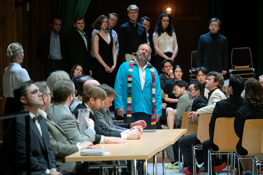 Am Sankt Johannistag öffnet Dr. Pogners Konservatorium seine Pforten allen interessierten Besucherinnen und Besuchern. Sie sitzen in der Aula des Konservatoriums. Seitlich rechts führt an der Wand entlang eine lange Tischreihe, an der die Lehrkräfte, Meister ihres Faches, platzgenommen haben.  Sachs steht am Kopfende der Tischreihe. Auf der Bühne der Aula hat ein Schülerchor unter Leitung von Magdalena Aufstellung genommen. 