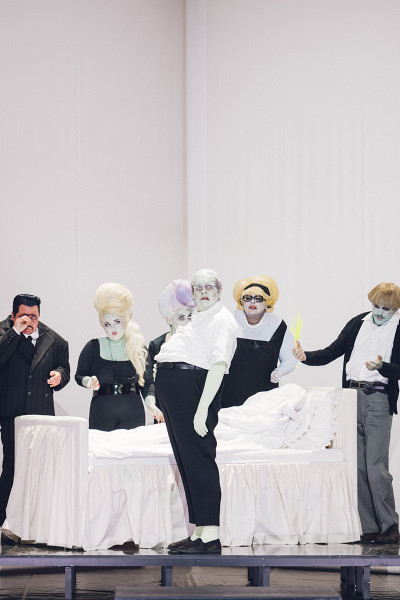 Gianni Schicchi - © Eike Walkenhorst Die Darsteller*innen haben grün oder gelb geschminkte Gesichter und Hände. Die Kostüme sind schwarz/weiß. Die Verwandtschaft - Gherardo, Marco, Zita, Simone, Nella - umstehen das Bett des Buoso Donati.