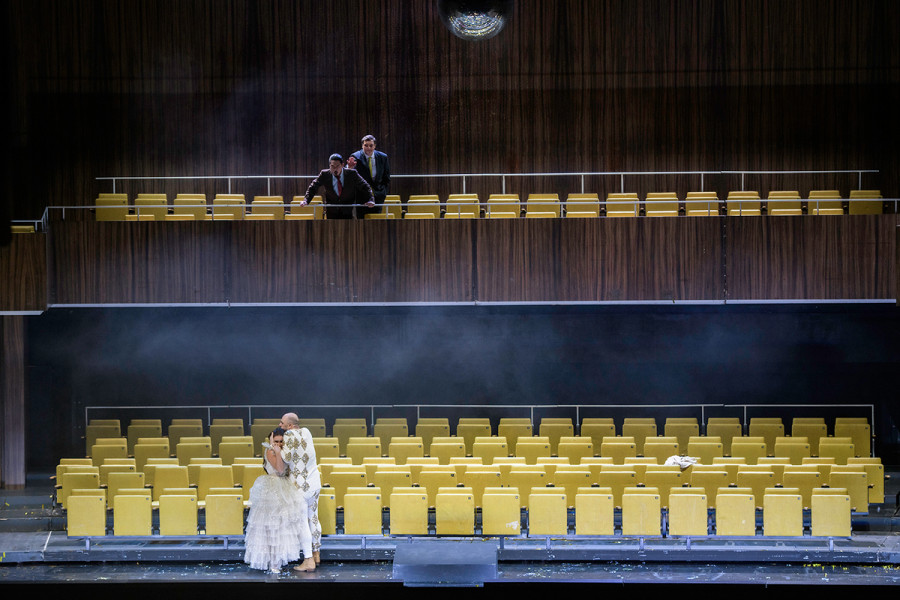 Rigoletto - © Bettina Stöß Rigoletto umarmt seine Tochter. In beider Gesichtern steht die Verzweiflung geschrieben. Aus dem ersten Rang schauen der Graf von Monterone, der Rigoletto dereinst verflucht hatte, und der Gerichtsdiener dieser Szene zu.