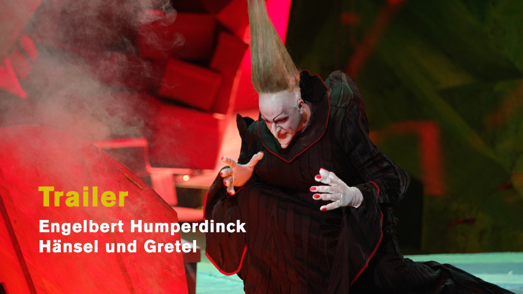 Engelbert Humperdinck: Hänsel und Gretel - © Ruth Tromboukis Dieses Foto ist das Standbild zum Videotrailer der Produktion. Darauf die Hexe, wie sie vor ihrem Häuschen die Tür zu ihrem Ofen geöffnet hat. Dichter Qualm steigt ihr entgegen. Ihr Blick ist gierig in den Ofen gerichtet.