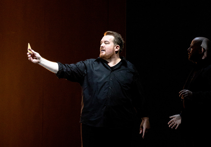 Tristan und Isolde -   © Bernd Uhlig  Tristan steht auf der Bühne, in den Händen ein gefaltetes Dokument. Neben ihm im Halbdunkel sein Freund Kurwenal.