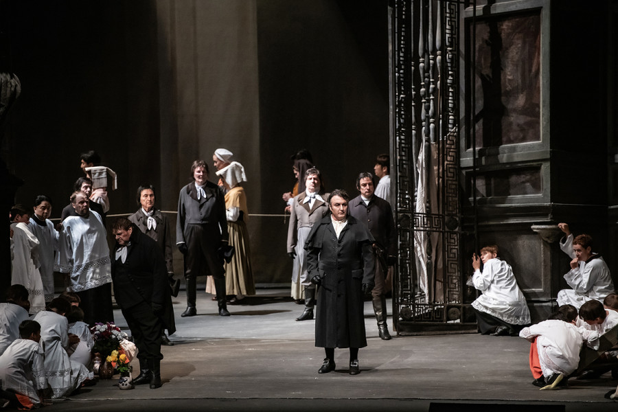 Tosca - © 2023, Bettina Stöß Der Auftritt von Scarpia und seinem Spion Spoletta verbreitet allenthalben Furcht und Schrecken. Scarpia trägt eine schwarze Pelerine, schwarze Strümpfe und schwarze Schnallenschuhe. Die Messdiener verstecken sich in den Ecken der Kirche und ducken sich zusammen.
