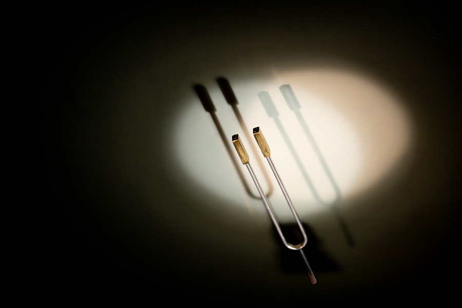 Spotlights - © Motiv: Georg Roither Eine Stimmgabel steht im Raum und wird von einem Scheinwerferlicht angestrahlt. Sie wirft einen klaren Schatten. Dieses Motiv illustriert das Kammerkonzert "Spotlights".