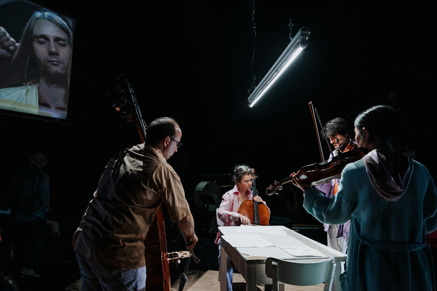 Satisfactionaction - © Nancy Jesse Am Küchentisch musizieren zwei Geiger, eine Cellistin und ein Kontrabassist.