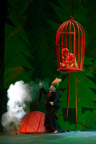 Hänsel und Gretel - © 2014 // Bettina Stöß Hänsel hängt in seinem Käfig in der Flugmaschinerie. Unter ihm steht die Hexe, die gerade den Grad der Mästung an der Fingerdicke des Knaben geprüft hat. Neben ihr ist der Hexenofen geöffnet.