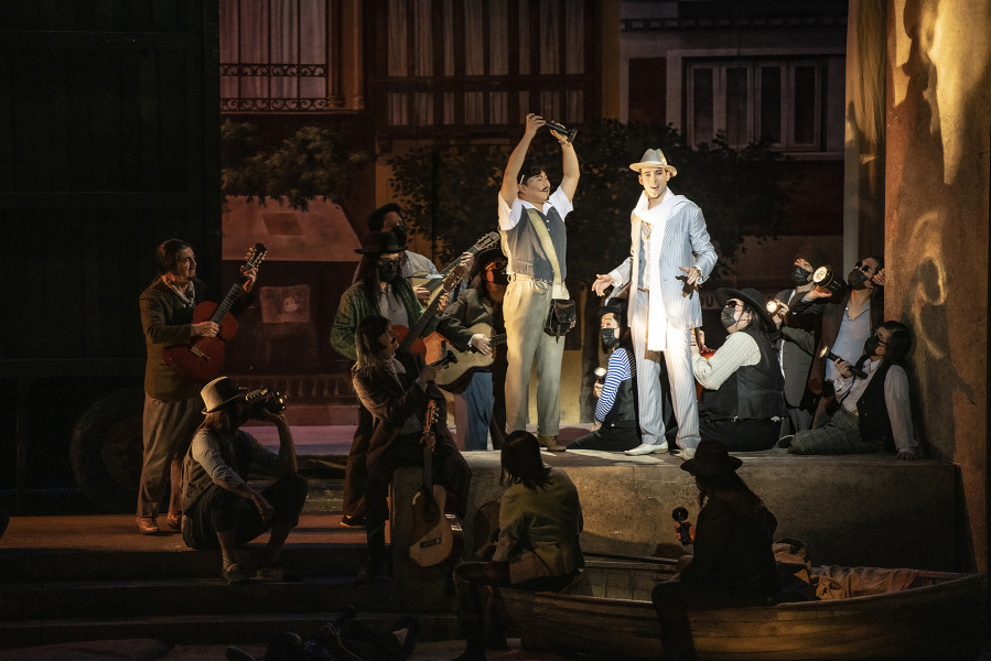 Il barbiere di Siviglia - © Bettina Stöß Graf Almaviva kommt in den Badeort. Neben Rosinas Theater-Wohnwagen singt er eine Canzonette. Er steht dabei auf einem Kaffeehaustisch. Die Herren des Chores und ein Gitarrist begleiten das Ständchen. Er trägt einen eleganten weißen Anzug und einen weißen Borsalino.