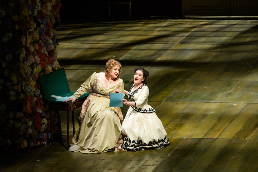 Le nozze di Figaro - © Bettina Stöß Susanna erzählt der Gräfin von der Verabredung mit dem Grafen im Garten. Die Gräfin diktiert einen Liebesbrief, den sie dann dem Grafen zustecken soll. Die beiden sind links im Bild an einem kleinen Sekretär. Das Bühnenportal ist mit Blumen dekoriert.