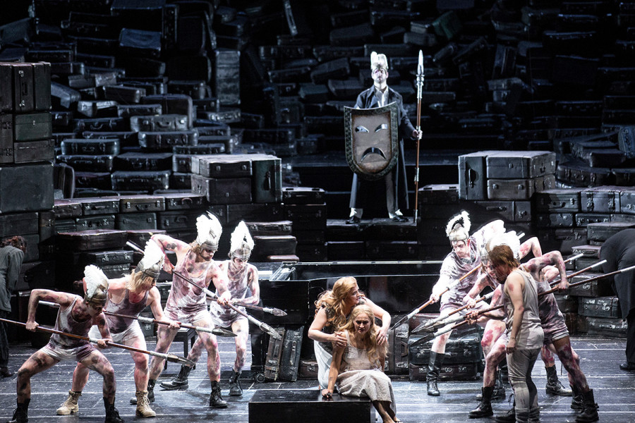 Die Walküre - © Bernd Uhlig Brünnhilde umarmt schützend die auf der Flucht verzweifelte Sieglinde. Helden, die auf den Schlachtfeldern rekrutiert wurden, um dereinst Wotans Burg gegen Alberich zu schützen, umgeben drohend die beiden Frauen. Hinter der Szenerie steht bereits Wotan.