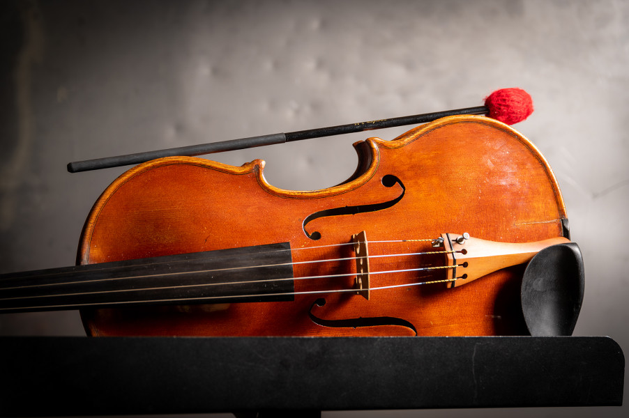 Auf dem illustrativen Foto liegt eine Violine auf der Seite. Darüber liegt ein Trommelschlägel.