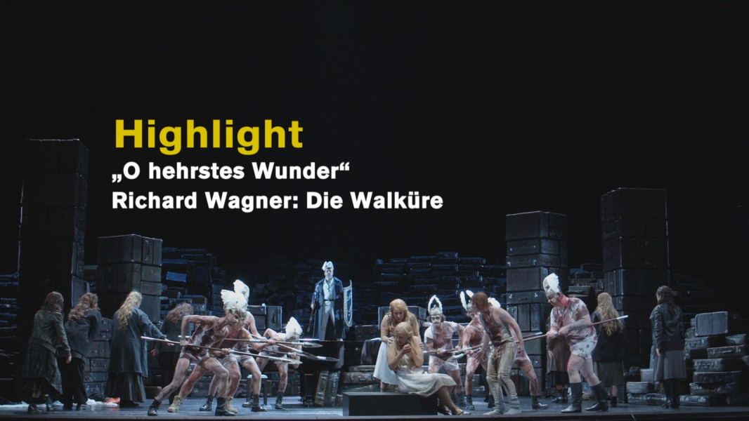 Lise Davidsen und Nina Stemme singen „O hehrstes Wunder“ aus DIE WALKÜRE - © Ruth Tromboukis Dieses Foto ist das Standbild zu einem Highlight-Video, in dem Nina Stemme und Lise Davidsen "O hehrstes Wunder" interpretieren. Auf dem Souffleur-Kasten sitzt Sieglinde, hinter ihr, sie schirmend, Brünnhilde. Einige der für Wotan von den Schlachtfeldern der Welt gesammelten Recken bedrohen die beiden Frauen mit den Lanzen. Die Walküren wenden sich ab. Im Hintergrund tritt Wotan auf.