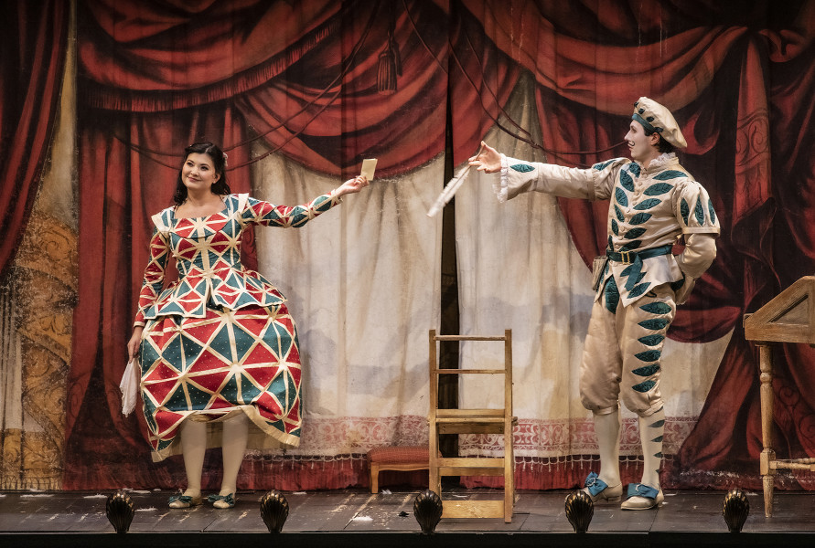 Il barbiere di Siviglia - © Bettina Stöß Rosina im typischen Gewand der Colombina mit großen roten und grünen Rauten überreicht Figaro ein kleines Brieflein.