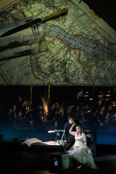 - Aida und Radames am Schreibtisch. Aida hat noch immer das Messer in der Hand. Auf der Leinwand über ihnen die Karte des Nilverlaufes und die Postkarte mit Sonnenuntergang.