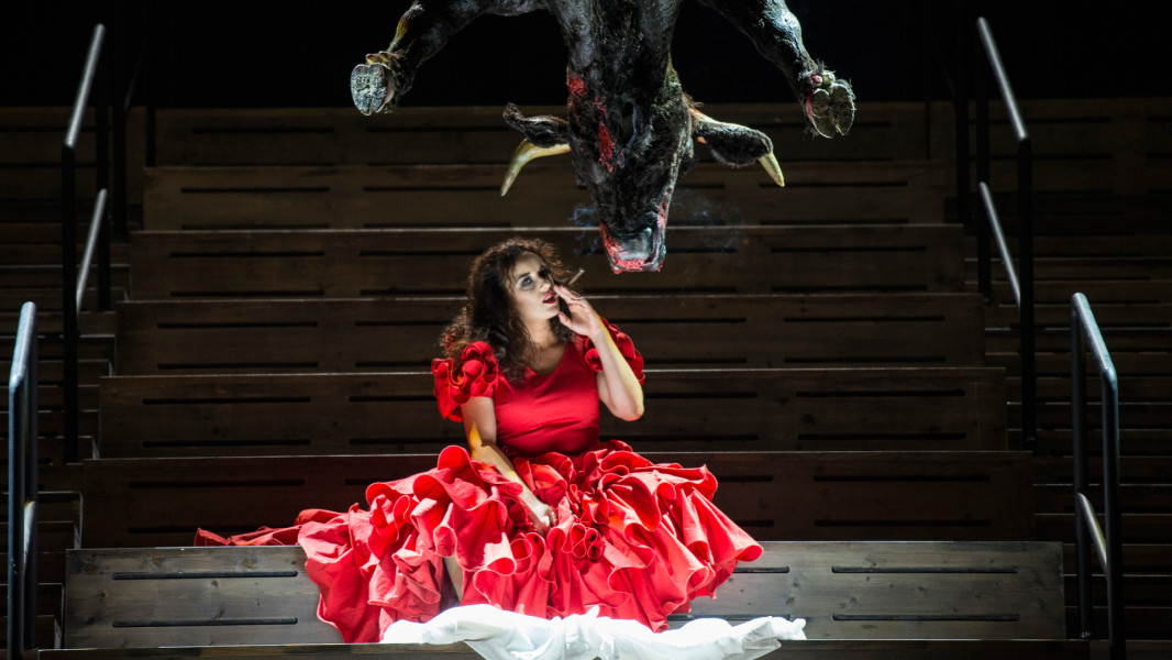 Carmen - © Marcus Lieberenz Carmen sitzt rauchend auf einer Treppe. Über ihr der Körper eines Stieres, der von der Decke hängt.