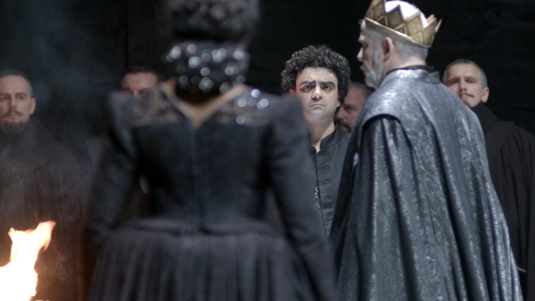 Don Carlo - © Ruth Tromboukis Dieses Foto ist das Standbild zu einem Videotrailer mit Stückimpressionen zu Marco Arturo Marellis Inszenierung von DON CARLO. Don Carlo steht Philipp II. und Elisabeth von Valois gegenüber. Philipp trägt Umhang und Krone, Carlos lediglich ein schwarzes Hemd.