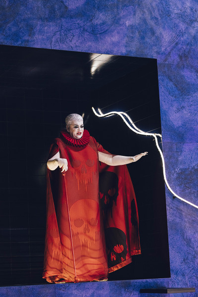 Suor Angelica - © Eike Walkenhorst La Zia Principessa in einem kleinen Raum (er ist auf der Rückseite des blauen Felsens eingelassen und kann durch Drehung des Bühnenbildsegments in den Vordergrund gebracht werden). Die Fürstin trägt ein langes rotes Kleid mit Totenköpfen. Die Haare sind sehr kurz, grau und nach hinten gebürstet. Sie hat einen roten Gehstock. Alles an ihr strahlt Härte aus.