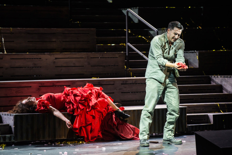 Carmen liegt tot auf der Bühne, Don José betrachtet seine blutigen Hände. Carmen trägt ein schweres rotes Kleid, dass spanisches Kolorit aufnimmt mit seinem Dekolleté und den vielen Volants. Don José trägt kakifarbene Militärkleidung.