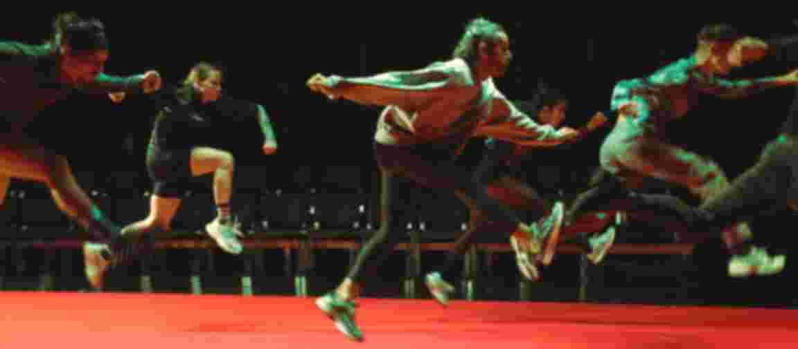 Fünf Tänzerinnen und Tänzer sind mitten im Flug festgehalten. Alle schweben in der Luft in der gleichen Bewegung in die gleiche Richtung.