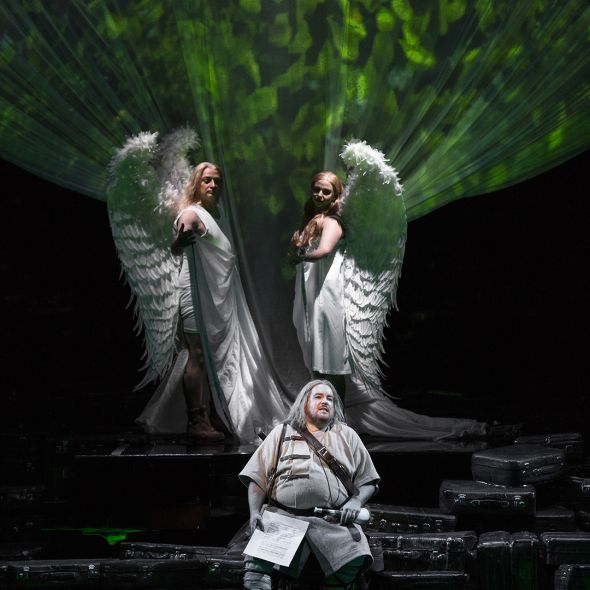 Eine Szenenimpression aus SIEGFRIED: Siegfried in einem das Mittelalter zitierenden Gewand. Hinter ihm als zwei Engel Siegmund und Sieglinde.