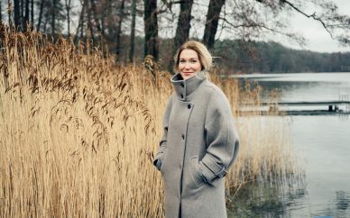 Sopranistin Maria Bengtsson am winterlichen Werbelliner See. Sie trägt einen grauen Wintermantel und steht nahe am Ufer. Hinter ihr Schilf. 