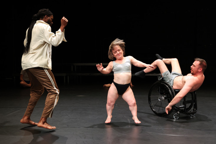 Drei Personen tanzen, eine von ihnen sitzt in einem Rollstuhl.