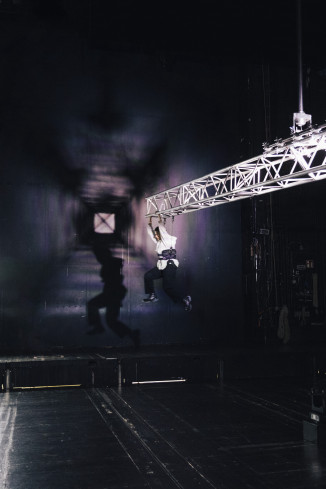 Eine Schauspielerin hängt an einem Pendel. Sie schwebt hoch in der Luft über dem Bühnenboden. Sie läuft in der Luft. 
