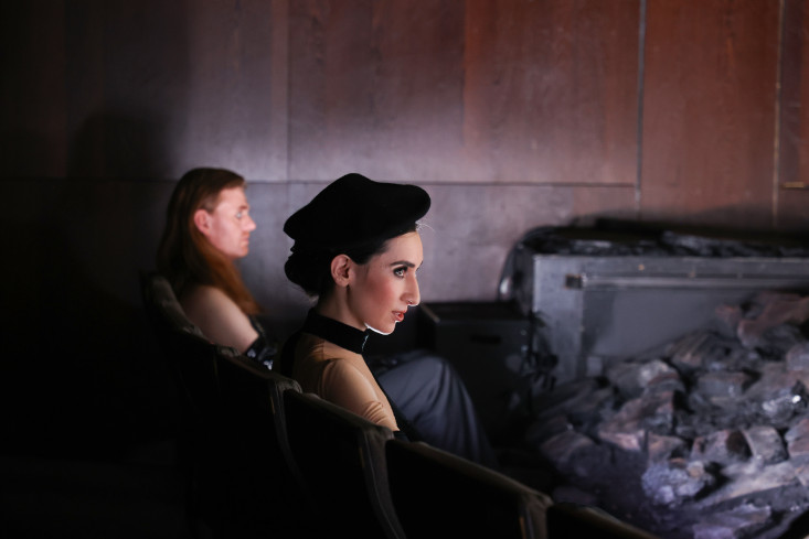 Ein Sänger und eine Sängerin sitzen in der ersten Reihe im Zuschauerraum. Sie blicken auf die Bühne. 